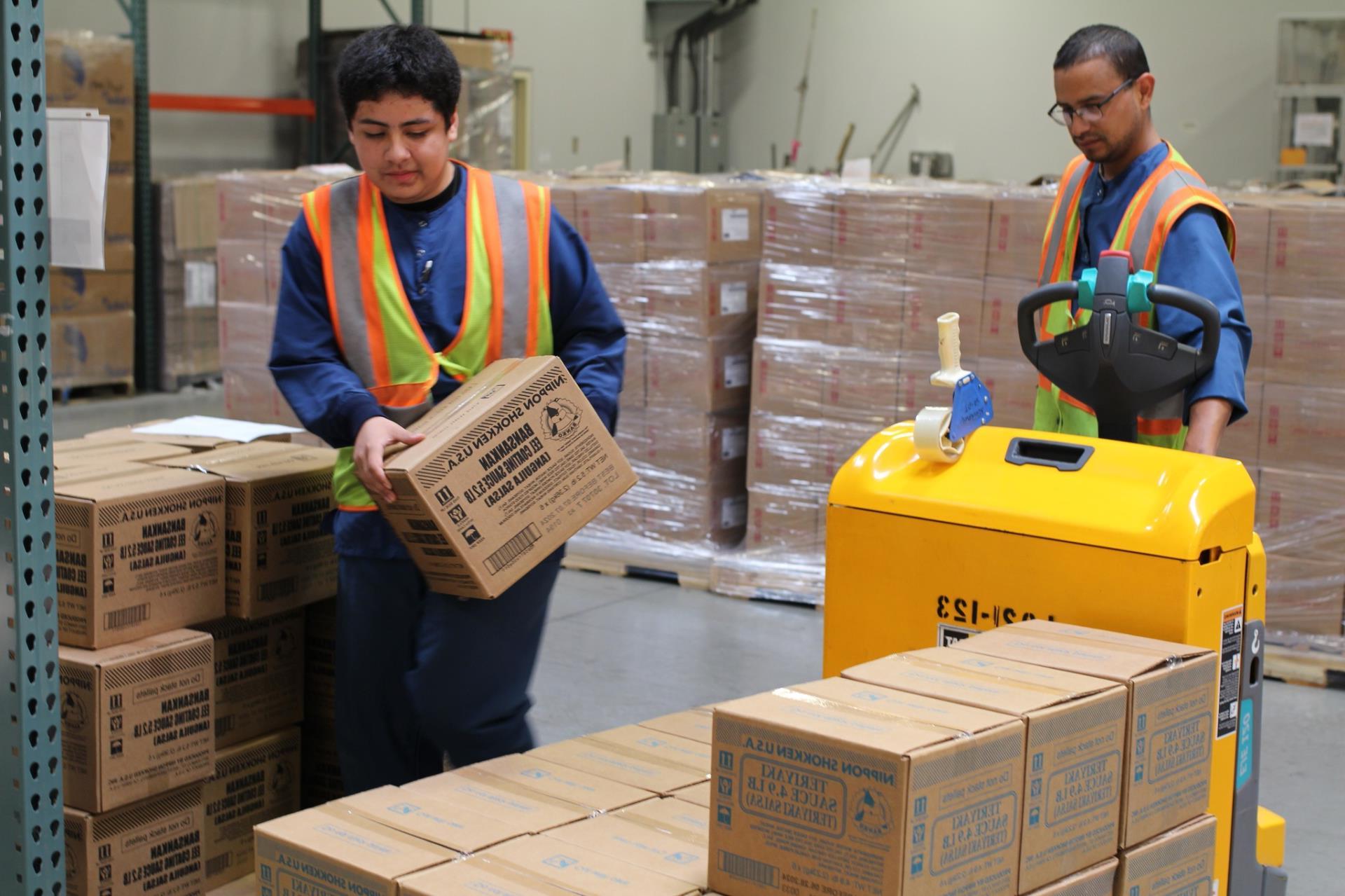 Two Male interns in safety vests moving boxes